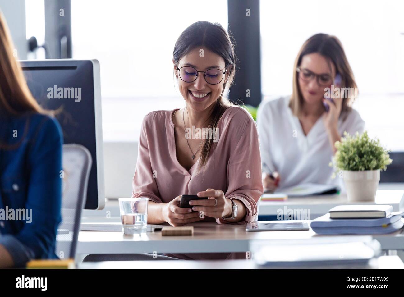 Lächelnde Geschäftsfrau, die im Büro das Smartphone überprüft Stockfoto
