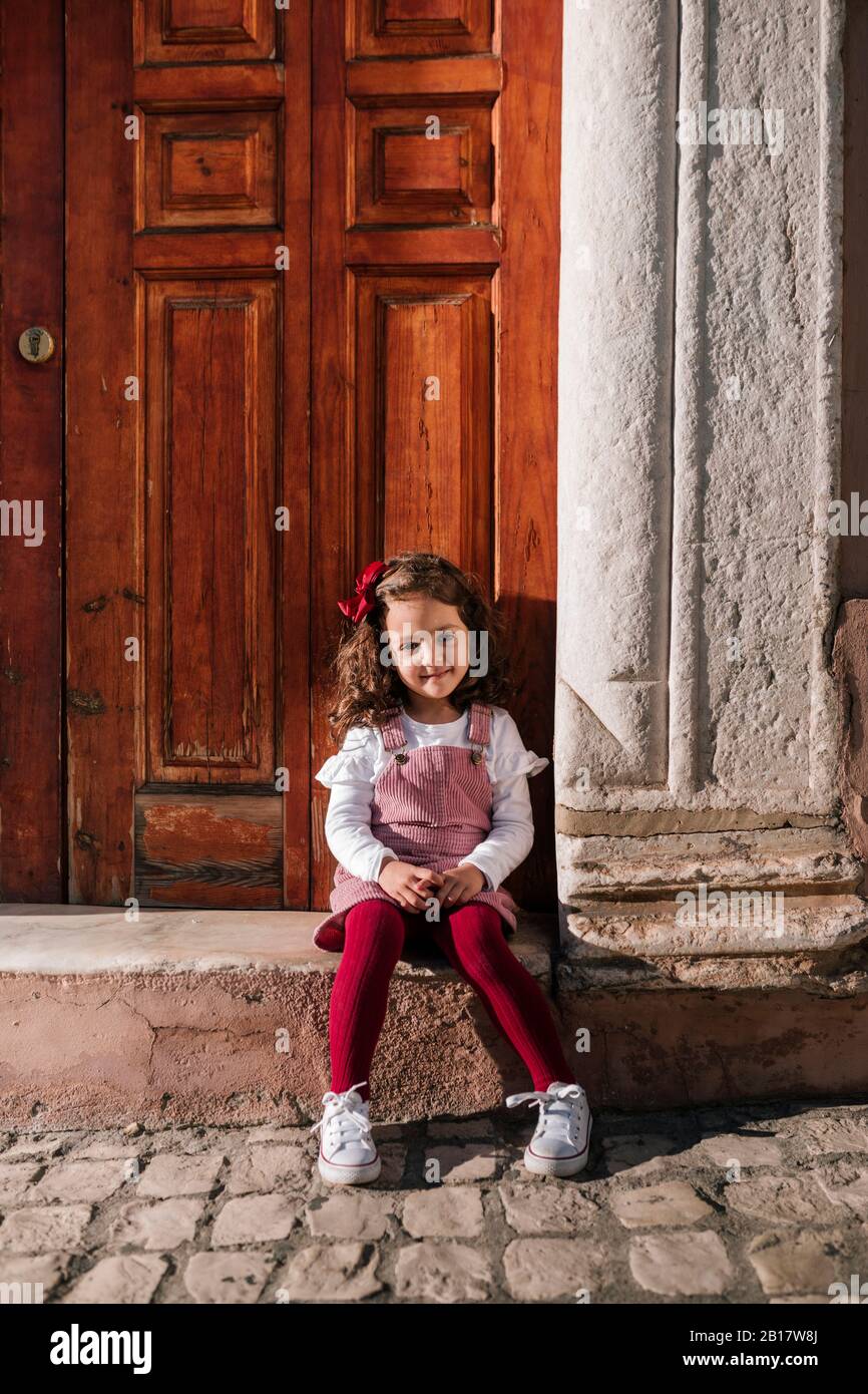 Porträt eines lächelnden Mädchens, das auf dem vorderen Stoop sitzt Stockfoto