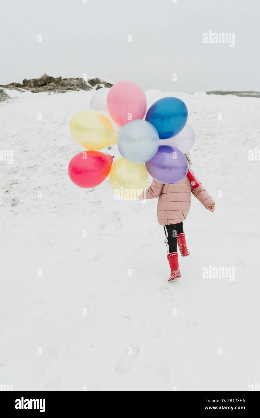 Rückansicht des Mädchens mit Ballons, die im Winter einen Hügel hinauf laufen Stockfoto