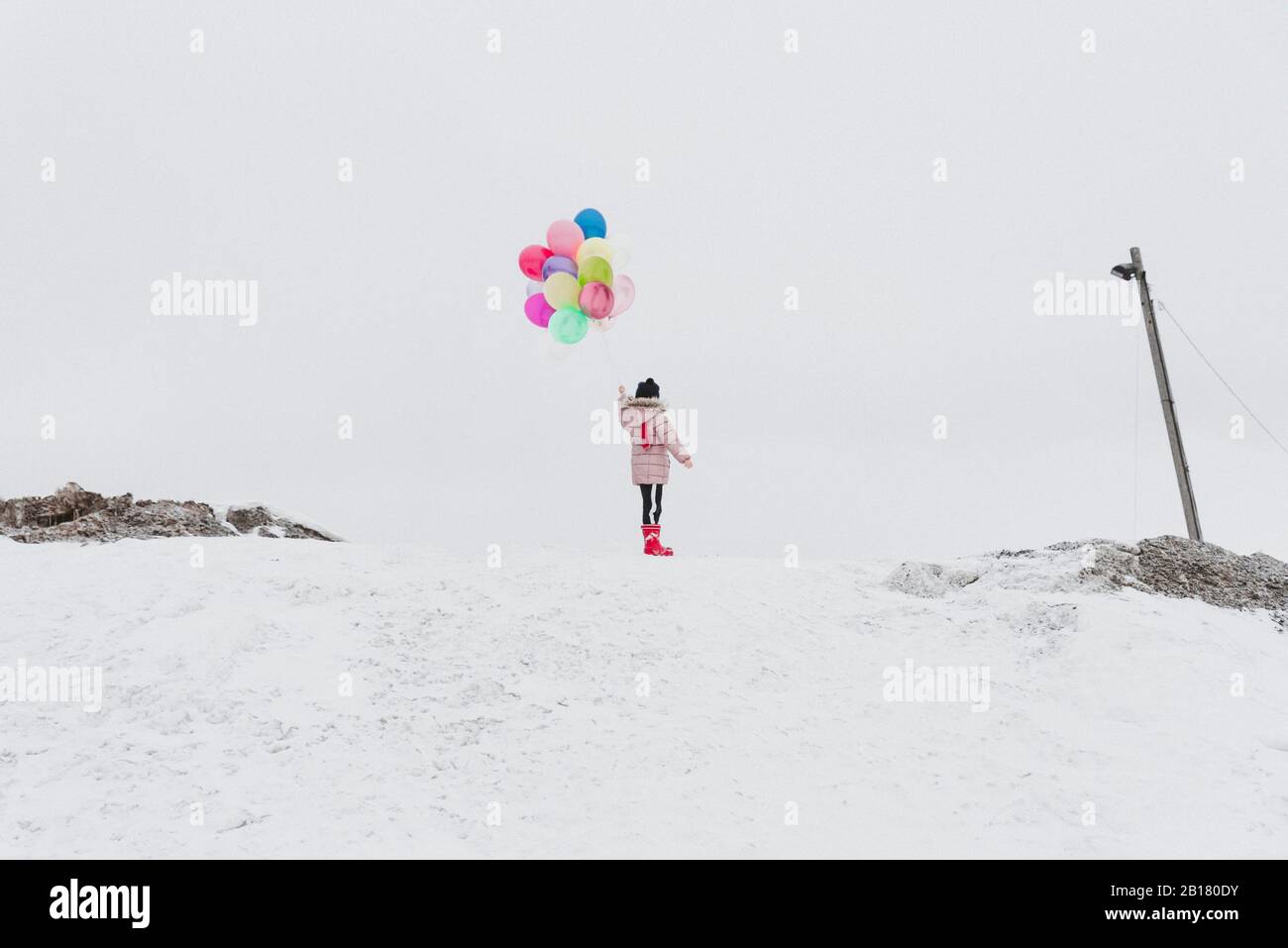 Rückansicht des Mädchens mit Ballons, die im Winter auf einem schneebedeckten Hügel stehen Stockfoto
