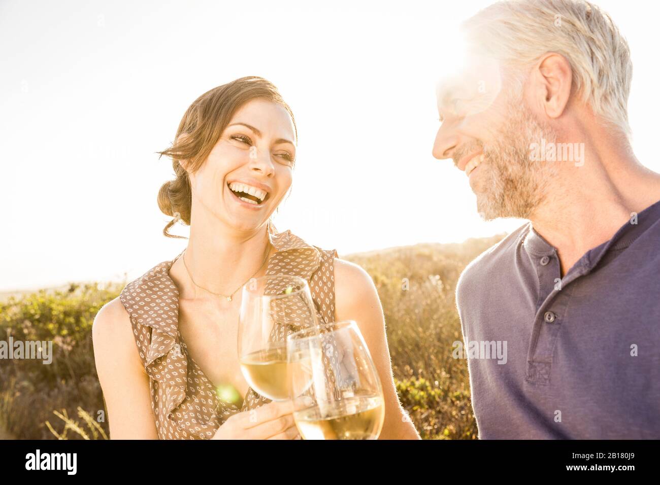 Glückliches Paar, das ein Glas Weißwein bei Sonnenuntergang hat Stockfoto