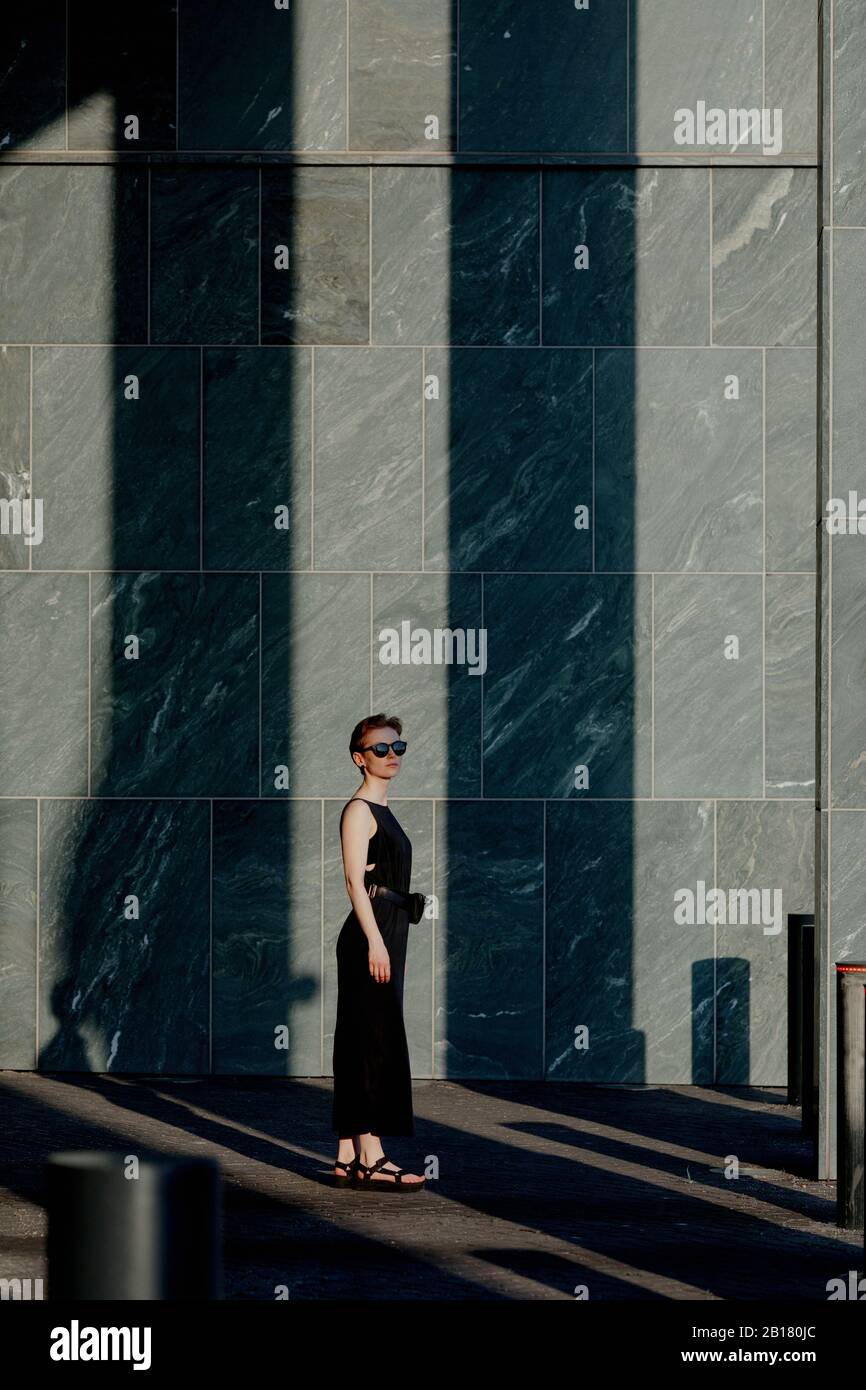 Rothaarige Frau mit Sonnenbrille, vor Steinwand mit Schatten Stockfoto