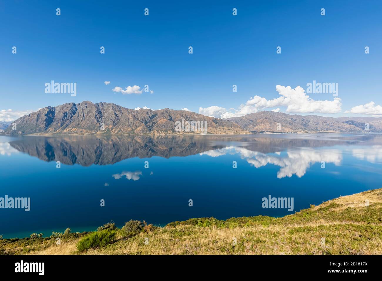 Neuseeland, Queenstown-Lakes District, Wanaka, Hills und blauer Sommerhimmel spiegeln sich im Lake Hawea Stockfoto