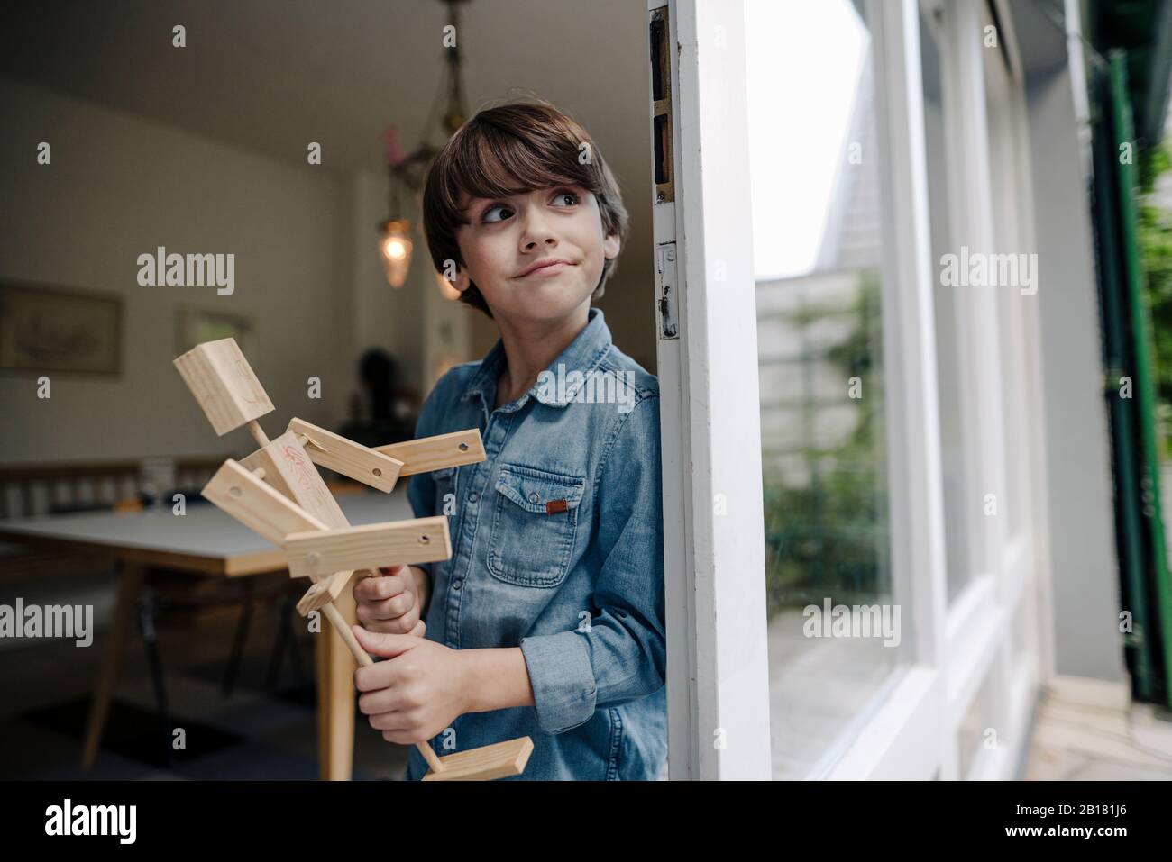 Kleiner Junge, der am Fenster steht und selbstgemachten Spielzeugroboter hält Stockfoto