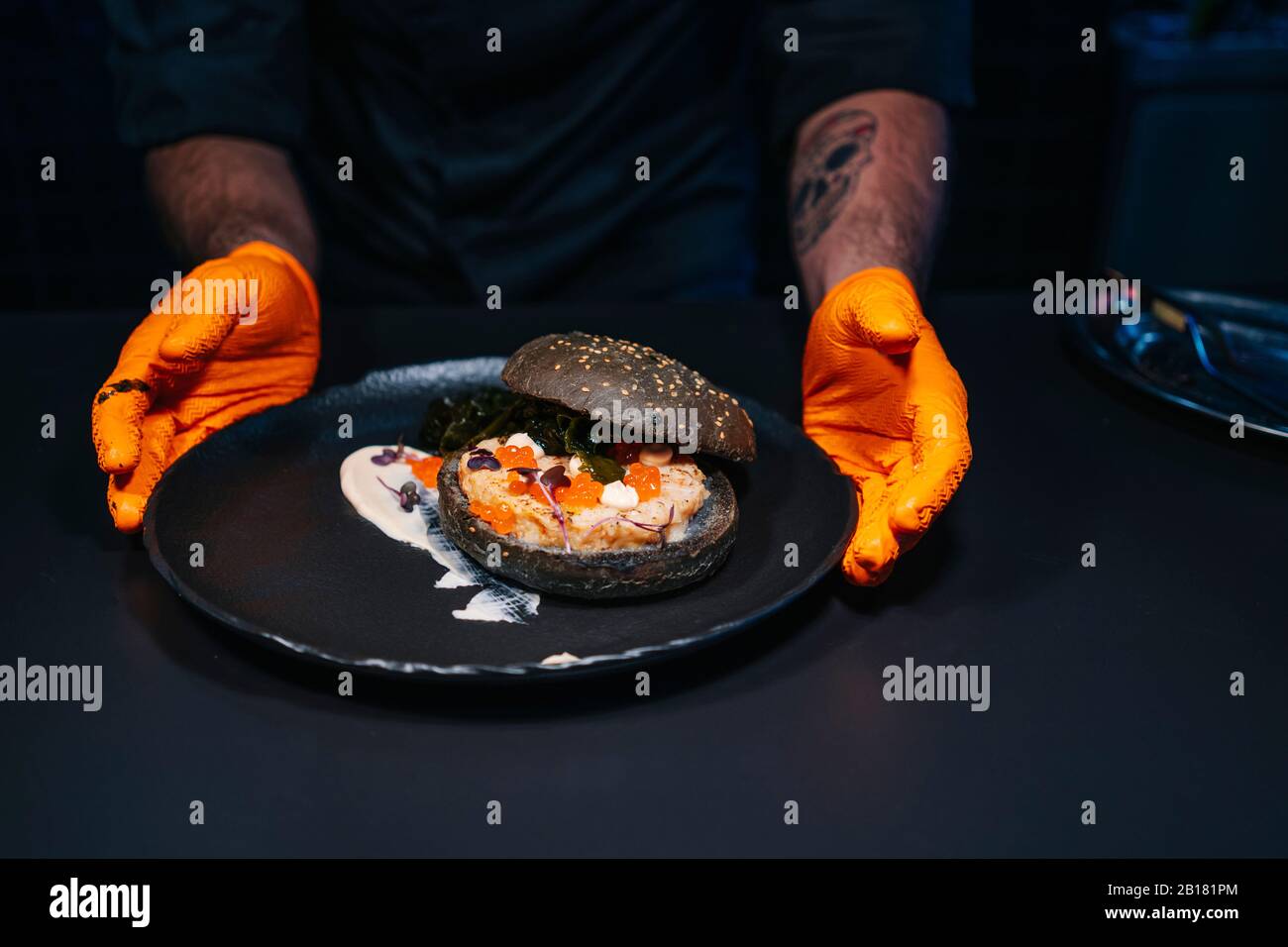Nahaufnahme des Küchenchefs, der ein Burger-Gericht in der Restaurantküche präsentiert Stockfoto