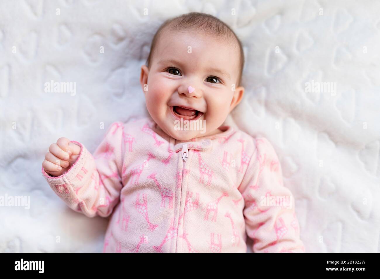Portrait des lachenden Mädchens mit rosa herzförmigen Süßigkeiten auf der Nase Stockfoto