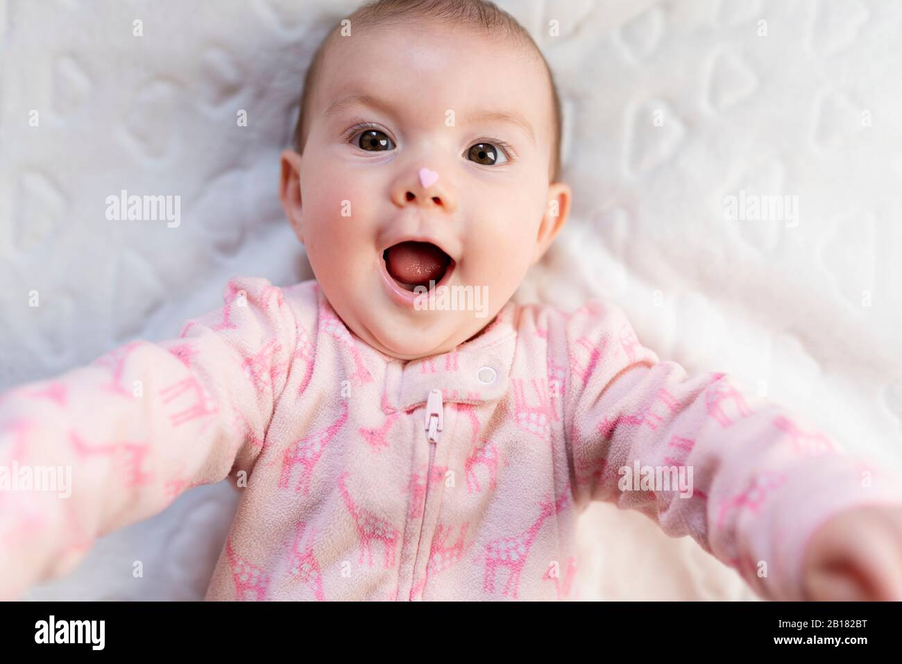 Portrait von Baby Mädchen mit rosa herzförmigen Süßigkeiten auf der Nase Stockfoto
