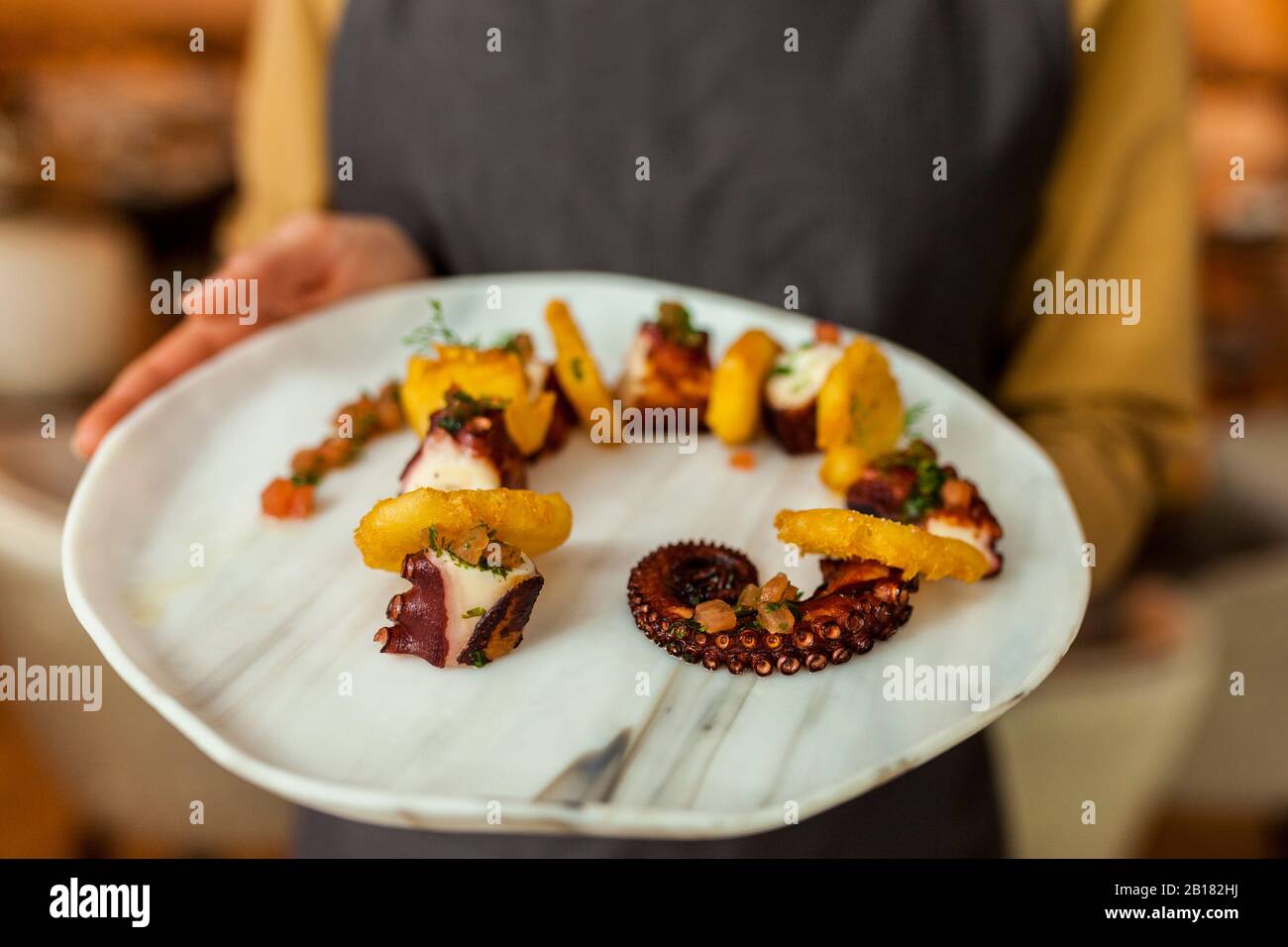 Kellnerin, die Kraken und Kartoffeln serviert Stockfoto