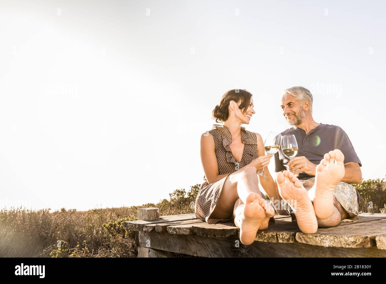 Fröhliches Paar, das an der Küste auf der Promenade sitzt und ein Glas Weißwein genießt Stockfoto