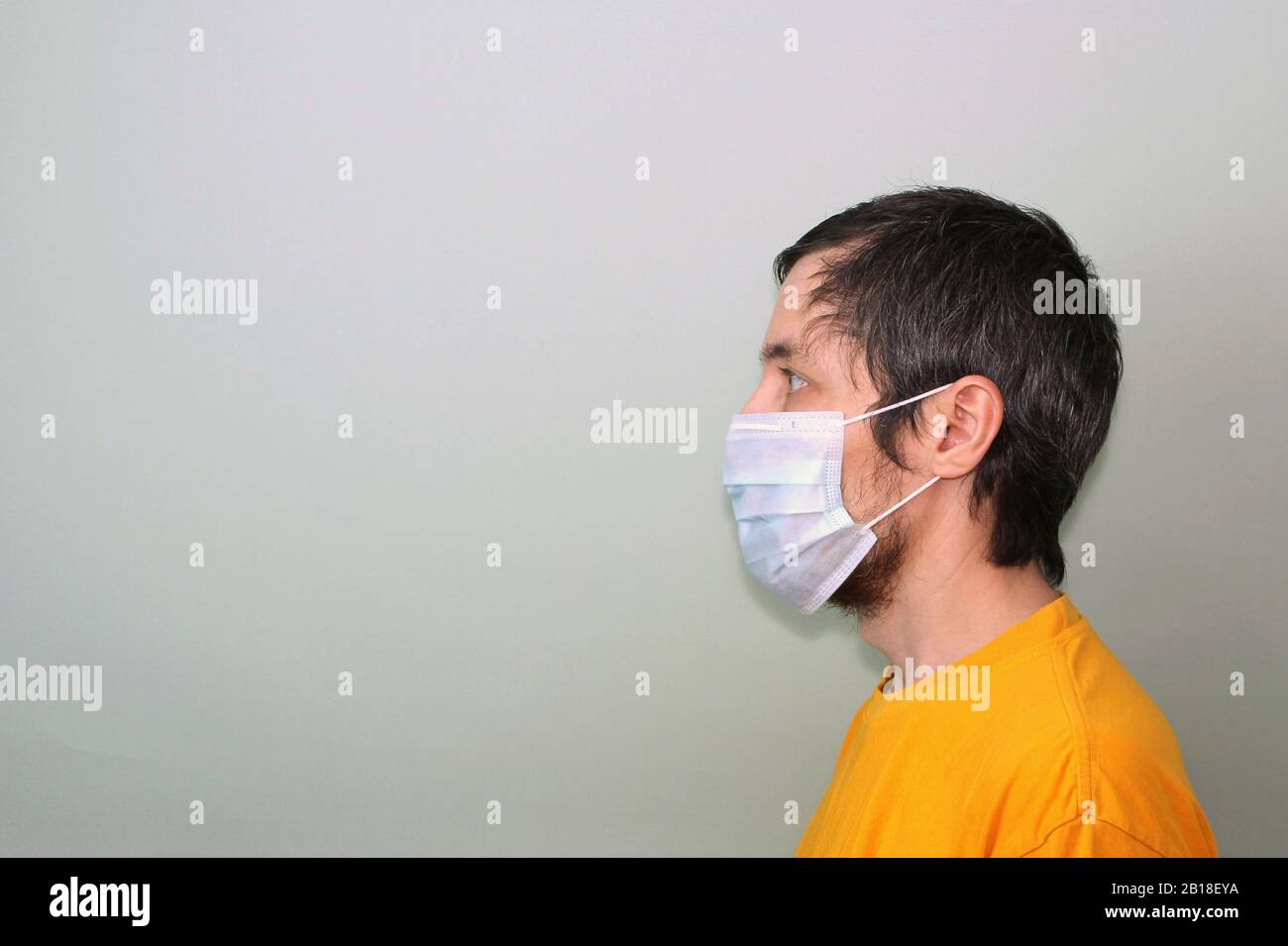 Erwachsener mittleren Alters in einem gelben T-Shirt auf grauem Hintergrund in einer medizinischen Maske seitlich im Profil. Krankheitsschutz Coronavirus epidemisches Problem aus China. Stockfoto