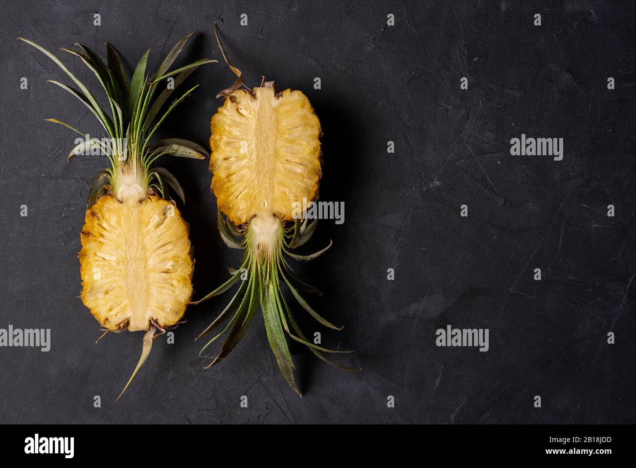Zwei Hälften frisch geschnittener Ananas auf schwarzem Hintergrund, Draufsicht mit Kopierraum Stockfoto