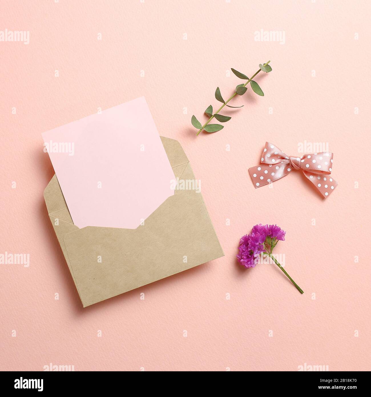 Kraft-Umschlag und leere Karte mit Statikblüte, Eukalyptusblätter auf pinkfarbenem Hintergrund. Blumendesign, flacher Lay, Draufsicht, Kopierbereich Stockfoto