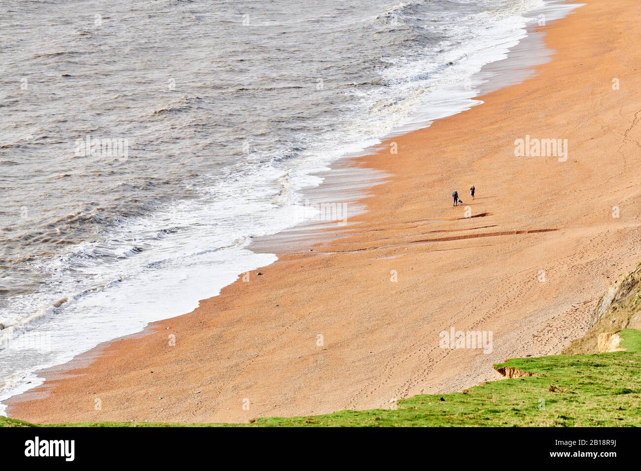 Spaziergänger am Schindelstrand in Seatown, Dorset, England, am Ärmelkanal, an einem sonnigen Wintertag. Stockfoto