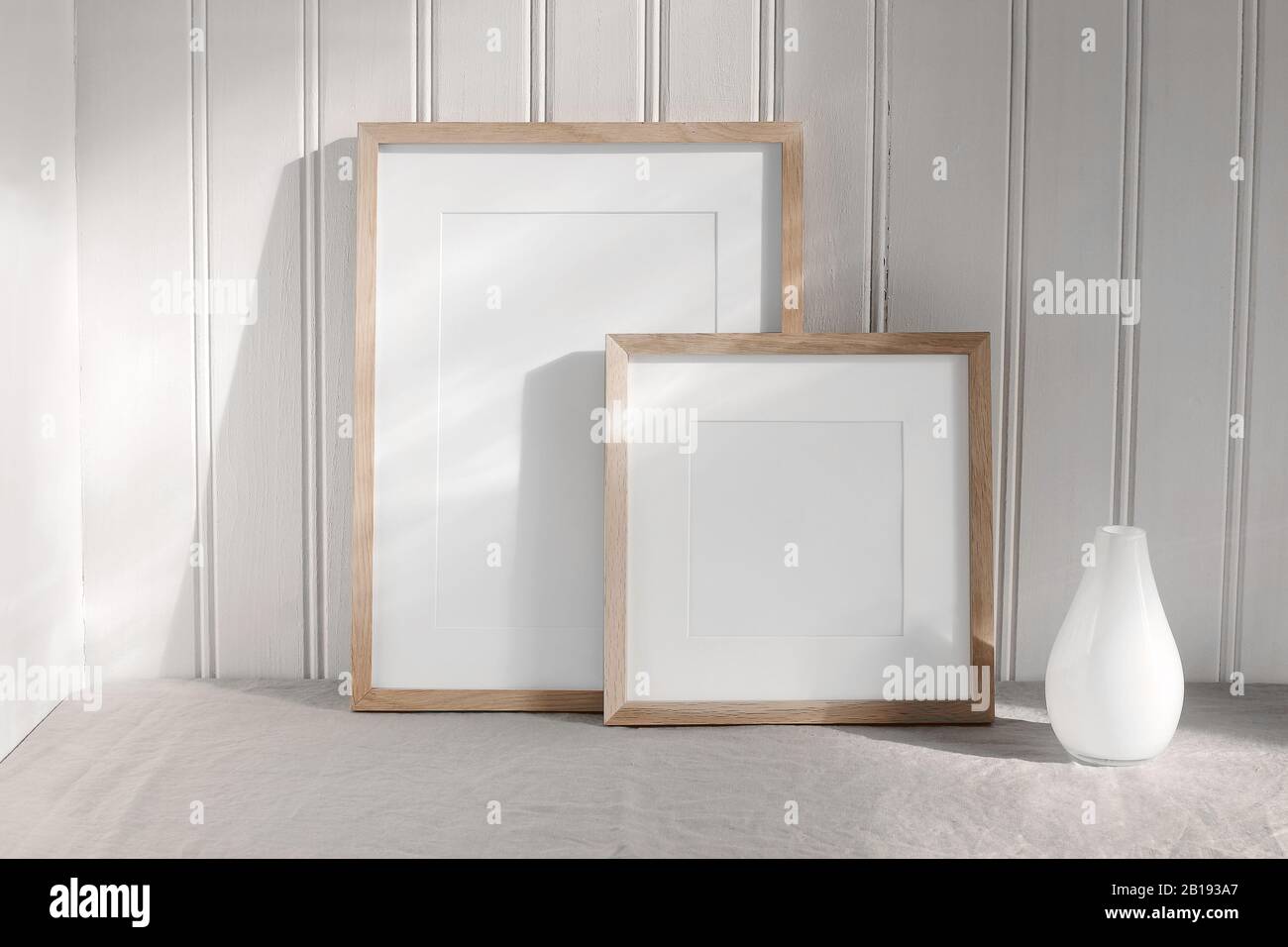 Zwei Mockups mit hoch- und quadratischem Holzrahmen. Leinentuch und moderne Keramikvase mit Sonnenlicht. Weiße Beadboard Wandverkleidung Hintergrund Stockfoto