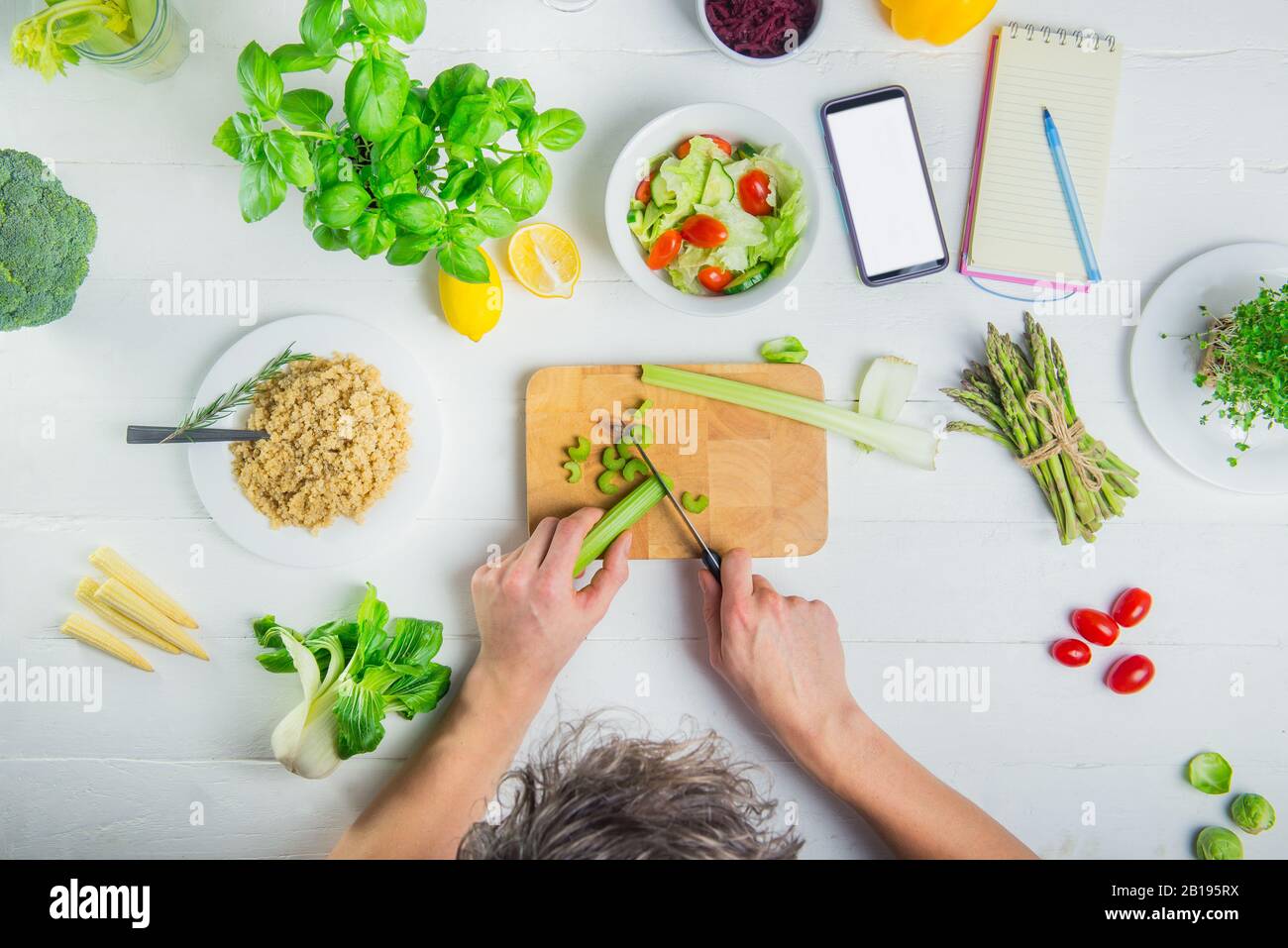 Man schneidet Sellerie und kocht veganen frischen Salat mit Gemüse. Leeres Smartphone und Notebook für die tägliche Diätplanung. Vegetarisch und vegan Stockfoto