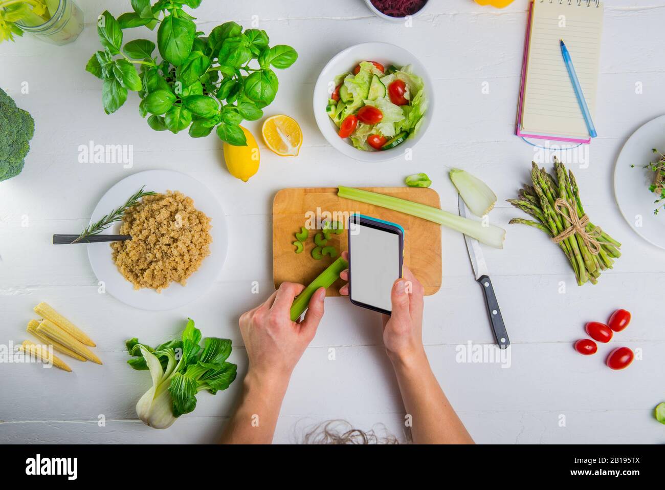 Draufsicht Man's Hands hält Smartphone mit leerem weißem Bildschirm und Selleriestab über dem Schneidebrett. Veganer frischer Salat mit Gemüse kochen. D Stockfoto