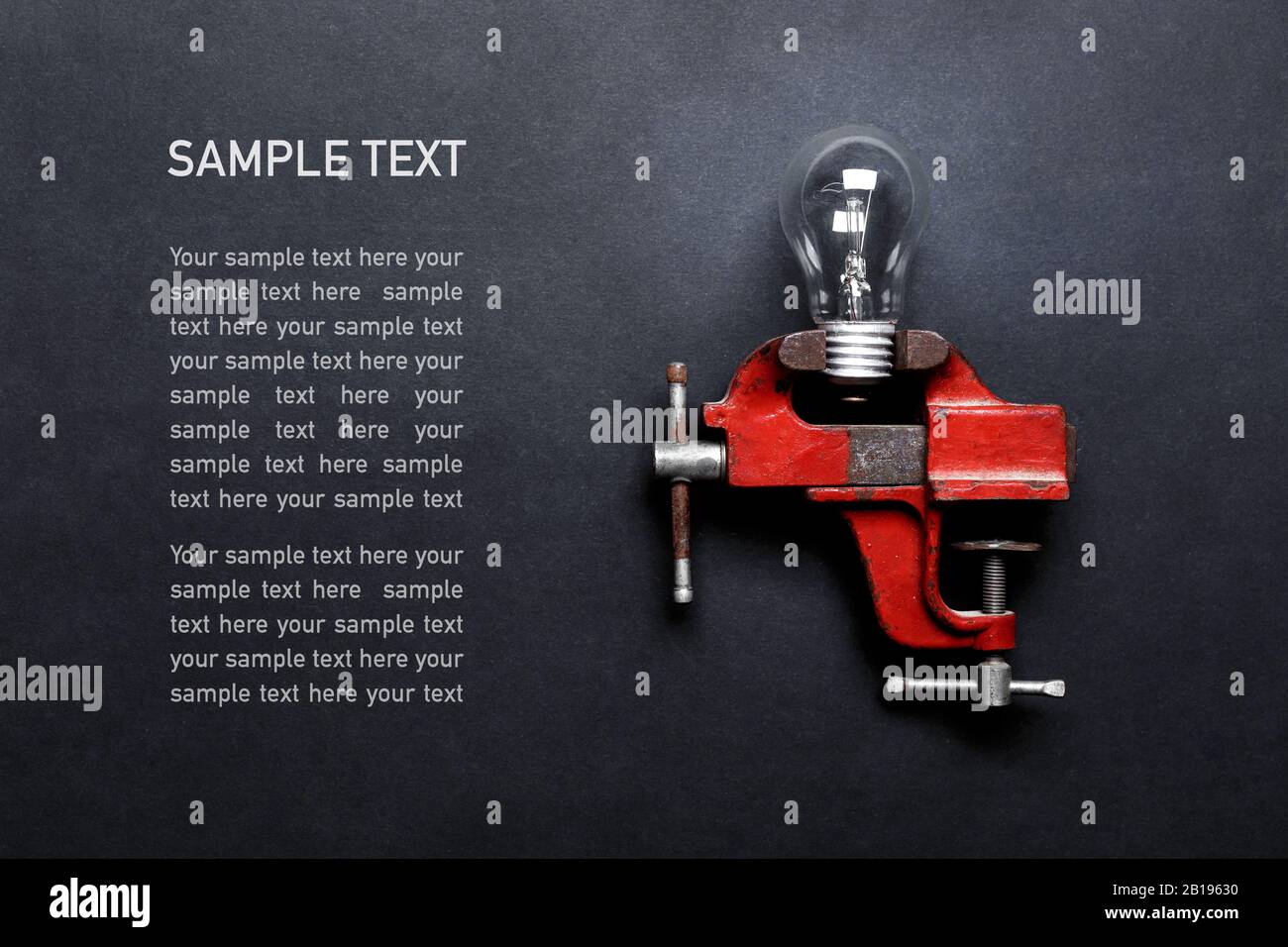 Glühlampe in mechanischer Handlaster auf grauem Hintergrund mit Kopierraum und Beispieltext eingeklemmt. Kreatives Designkonzept Stockfoto