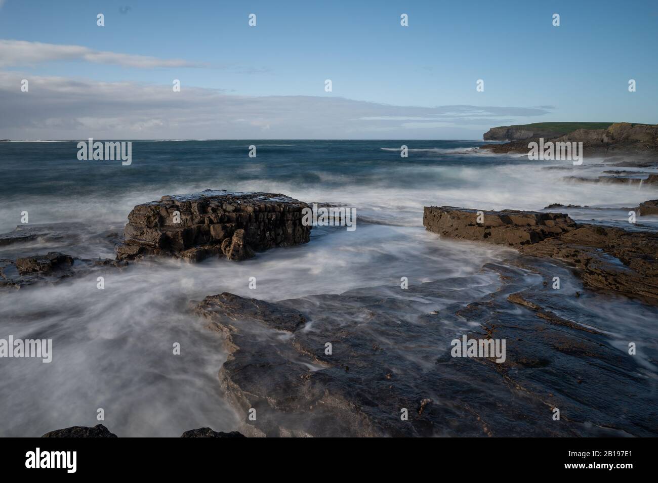 Ein relativ ruhiger Tag in Kilkee, wo die Wellen gegen die Felsen brachen. Stockfoto