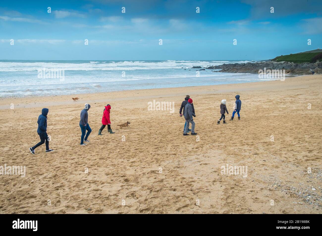 Menschen, die einen zügigen Spaziergang bei dem kühlen, windigen Wetter am Fistral Beach in Newquay in Cornwall genießen. Stockfoto