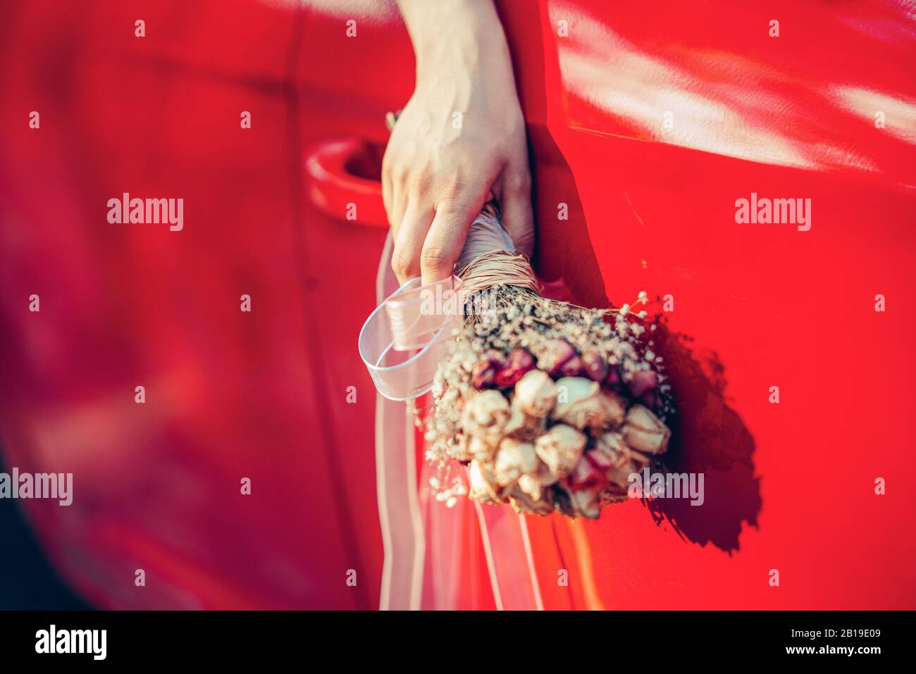 Die Braute, die den Blumenstrauß hält, winkelt ihn aus dem Fenster des roten Autos Stockfoto