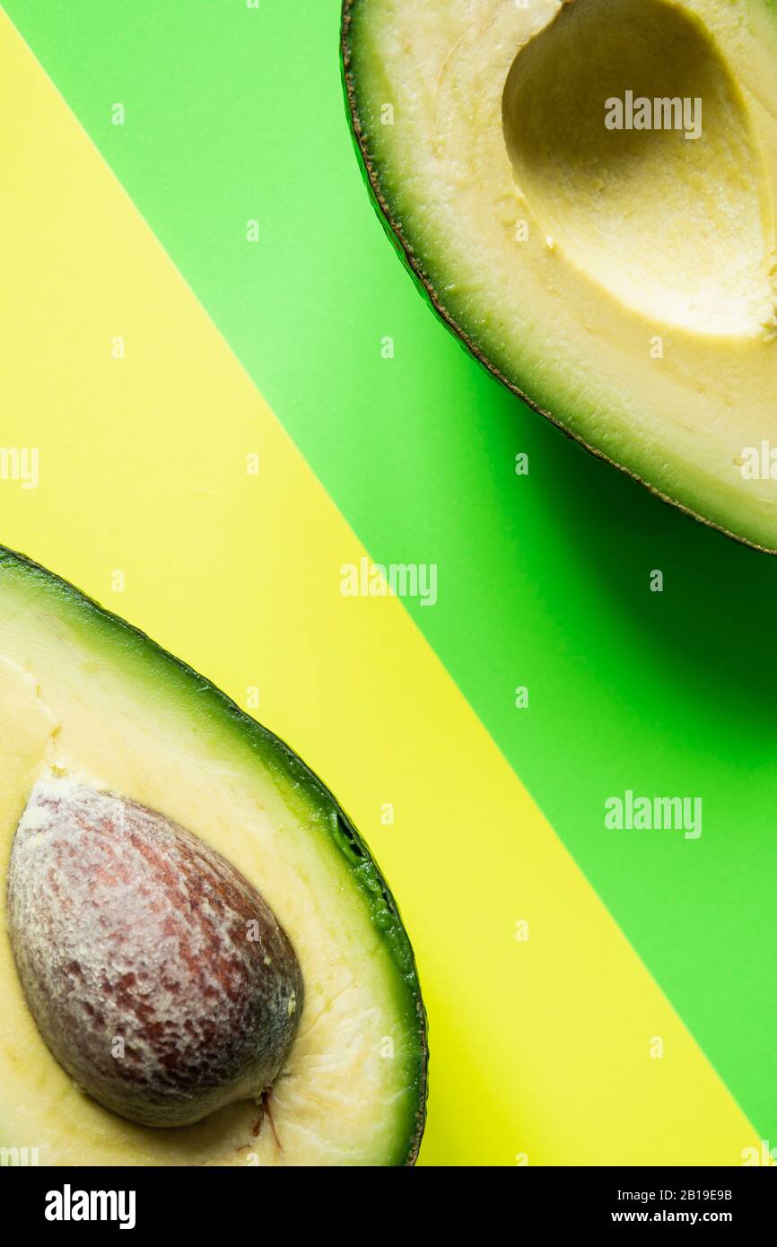 Bereit zum Essen Avocado in zwei Hälften geschnitten, isoliert auf grünem und gelbem Hintergrund. Stockfoto