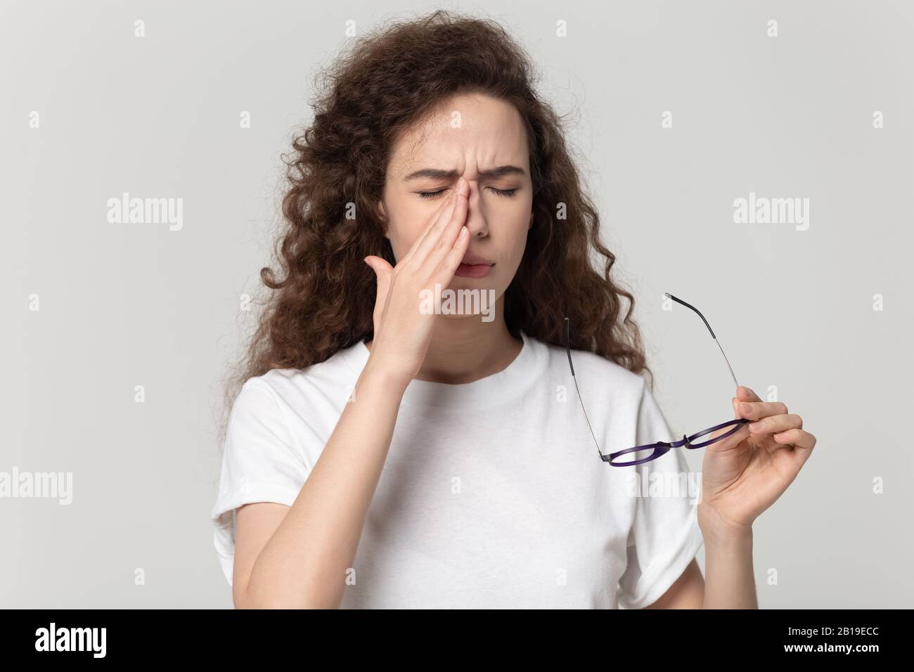 Müde junge Frau, die Augenspülung abfällt und an einem trockenen Augensyndrom leidet. Stockfoto