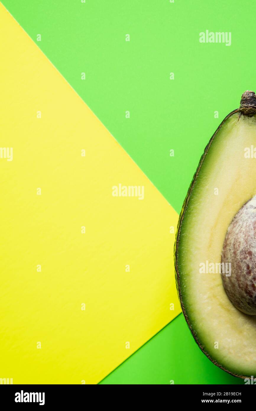 Bereit zum Essen Avocado in zwei Hälften geschnitten, isoliert auf grünem und gelbem Hintergrund. Stockfoto