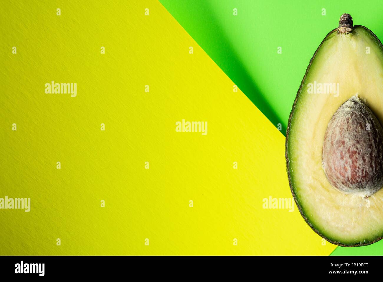 Bereit zum Essen Avocado in zwei Hälften geschnitten, isoliert auf grünem und gelbem Hintergrund. Stockfoto