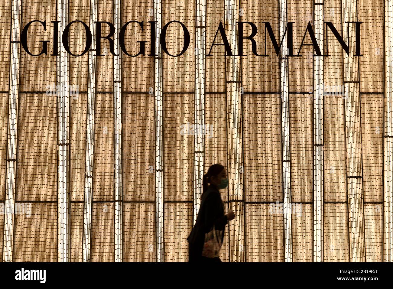 Ein Fußgänger, der eine Gesichtsmaske trägt, läuft am Giorgio Armani Markenladen und Logo in Hongkong vorbei.Das tödliche Coronavirus (bekannt als COVID-19) hat die meisten Industrien, Fabriken und Einkaufszentren in China zum Stillstand gebracht. Mehr als 50 Millionen Menschen unter Quarantäne. Länder beschränken sich auf Einträge, um die Verbreitung des Virus zu kontrollieren. Sowie mehr als 25.000 Flugausfälle weltweit. Viele Länder können keinen Rohstoff aus China holen. Lange Zeit abhängig von den Ausgaben der chinesischen Käufer erinnern nach Hause. Der Luxusgüterkonzern Herms wird Investoren am Mittwoch, 26. Februar 2019 eine Aktualisierung zur Verfügung stellen. Analysten Stockfoto