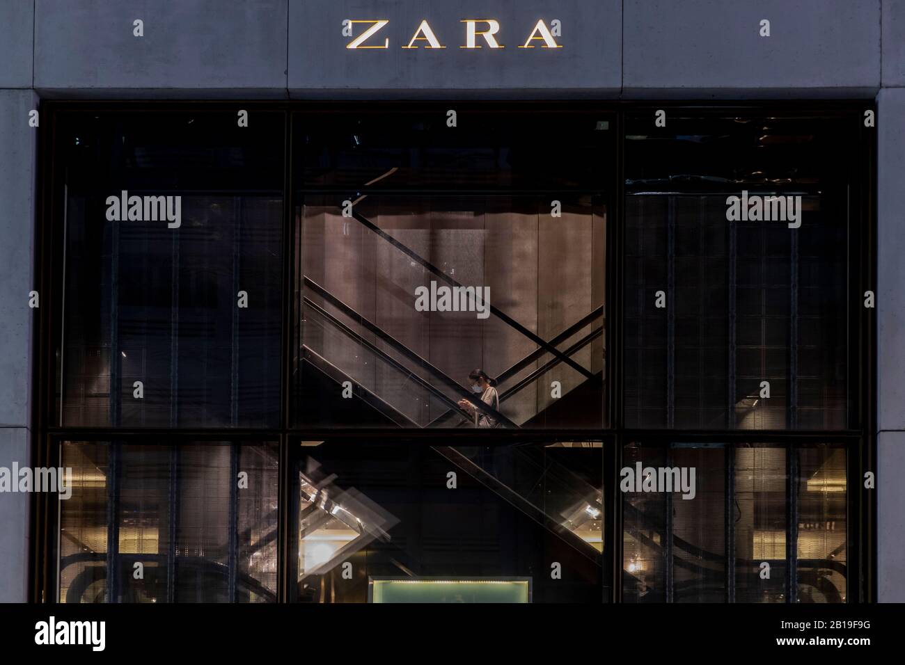 Ein Fußgänger, der eine Gesichtsmaske trägt, läuft am Zara-Markenladen und dem Logo in Hongkong vorbei.Das tödliche Coronavirus (COVID-19) hat die meisten Industrien, Fabriken und Einkaufszentren in China zum Stillstand gebracht. Mehr als 50 Millionen Menschen unter Quarantäne. Länder beschränken sich auf Einträge, um die Verbreitung des Virus zu kontrollieren. Sowie mehr als 25.000 Flugausfälle weltweit. Viele Länder können keinen Rohstoff aus China holen. Lange Zeit abhängig von den Ausgaben der chinesischen Käufer erinnern nach Hause. Der Luxusgüterkonzern Herms wird Investoren am Mittwoch, 26. Februar 2019 eine Aktualisierung zur Verfügung stellen. Analysten haben warne Stockfoto