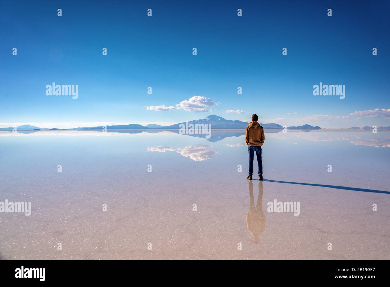 Junger Mann, der die Landschaft und den Miror-Effekt in Salar de Uyuni (Uyuni-Salzwohnungen), Potosi, Bolivien, Südamerika beobachtet Stockfoto