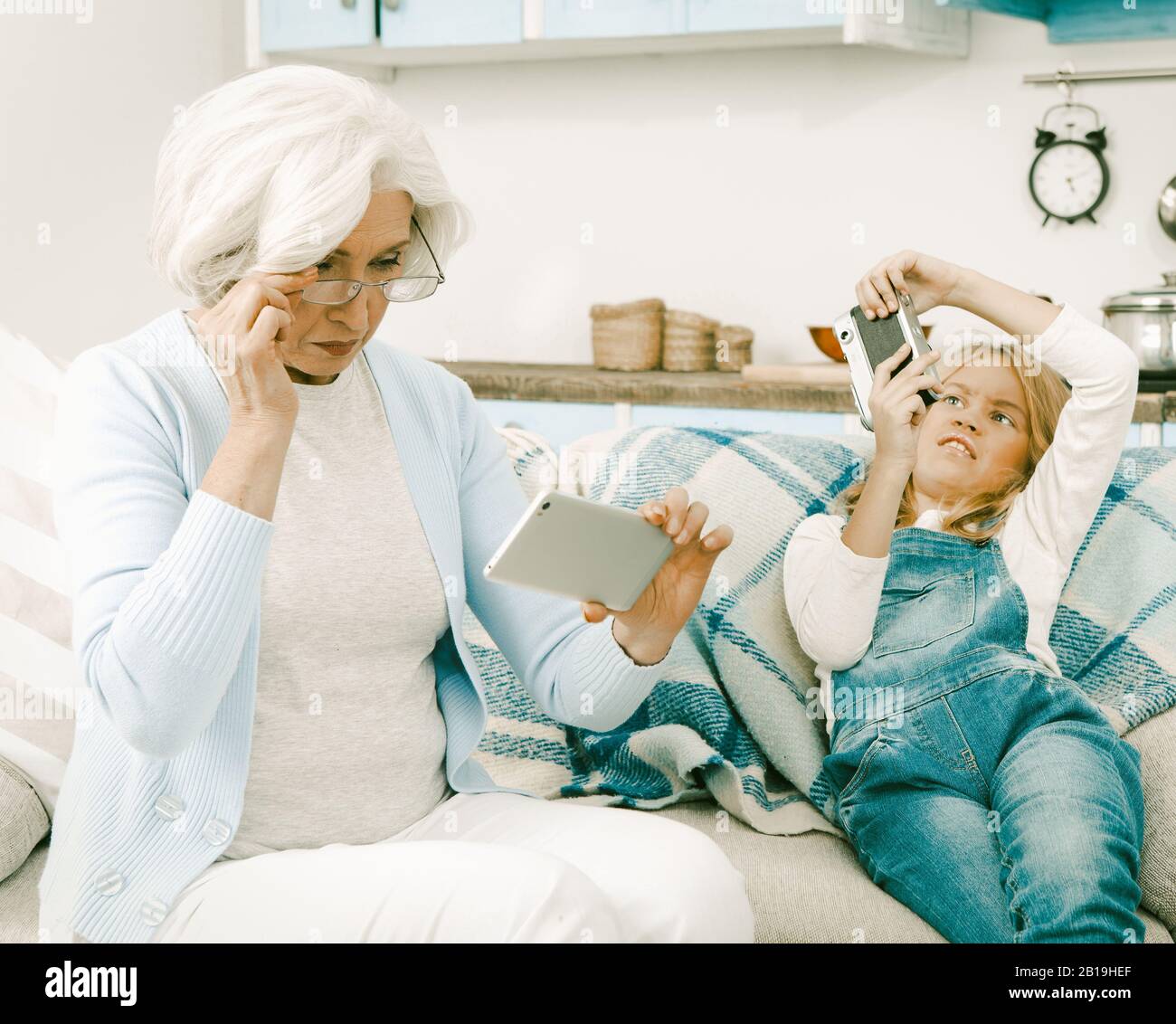 Großmutter Und Enkelin, die in Ungezwungener Atmosphäre gekredelt Wurden, Verwenden Die Gadgets Des Anderen, Um Selfie Pictures Zu Nehmen, Während Sie Auf Sofa Oder Sofa Zu Hause Sitzen Stockfoto