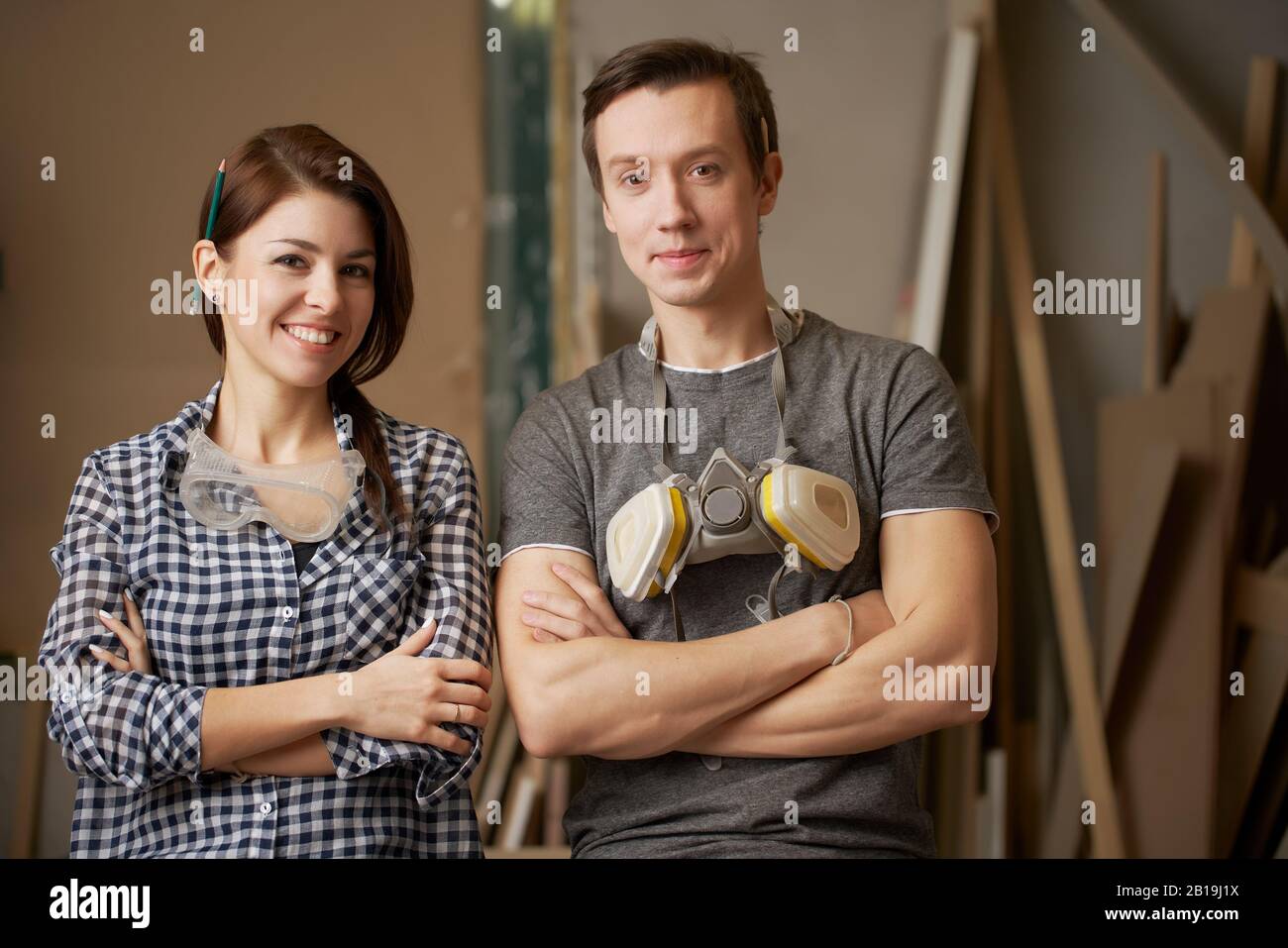 Lächelnde Männer- und Damenfugen mit in der Werkstatt gekreuzten Armen Stockfoto