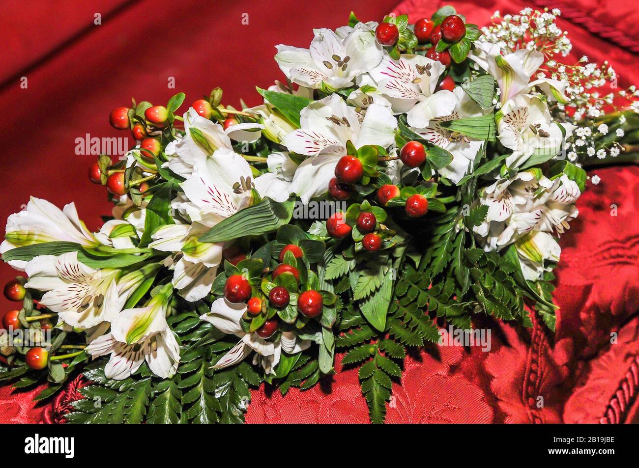 Bouquet von weißen Lilien mit Flecken und roten Früchten auf rotem Tuch. Lilium 'Stargazer. Stockfoto