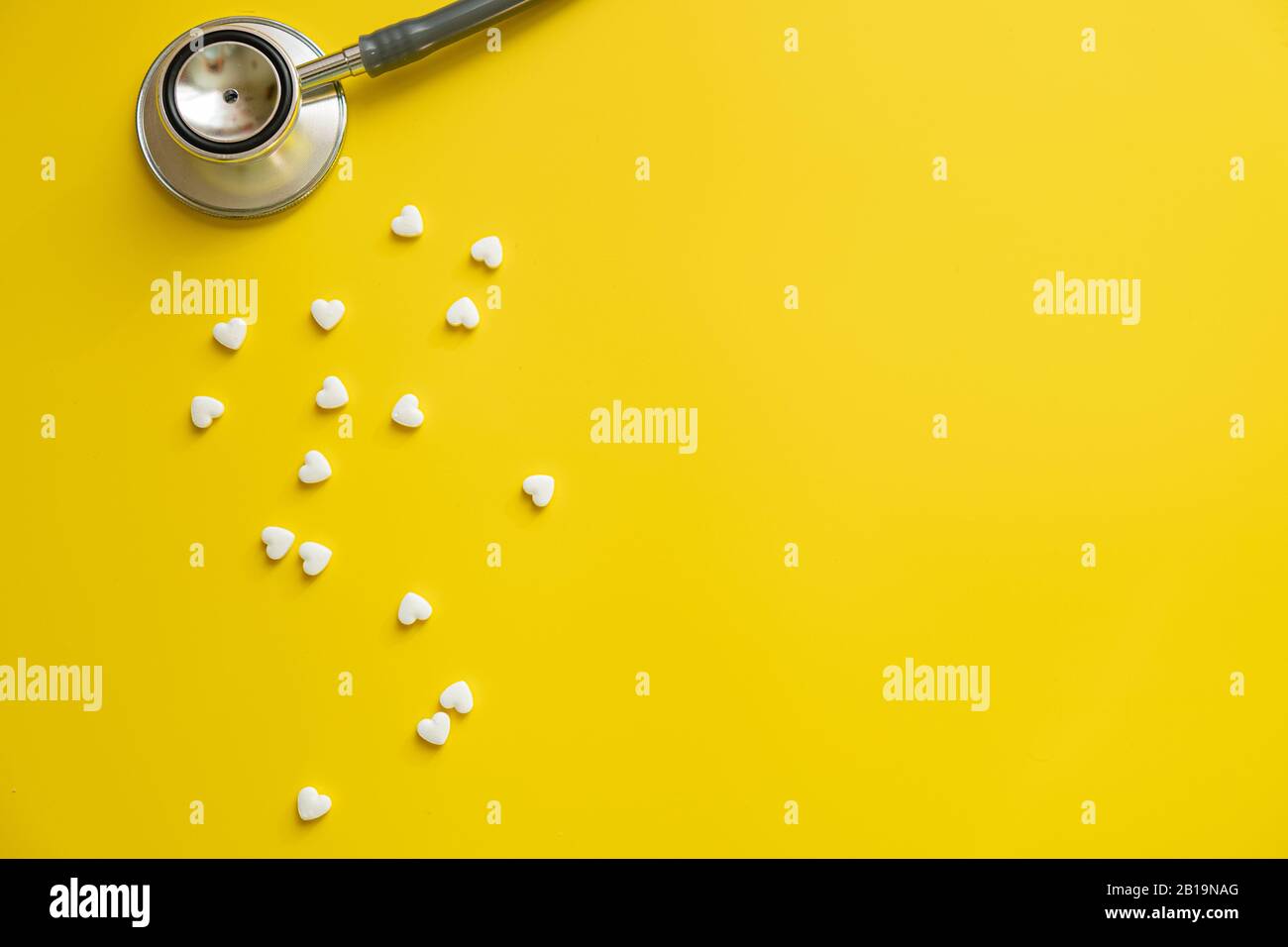 Medizinisches Stethoskop und weiße Herzpillen auf gelbem Hintergrund Gesundheitsminimalismuskonzept Stockfoto