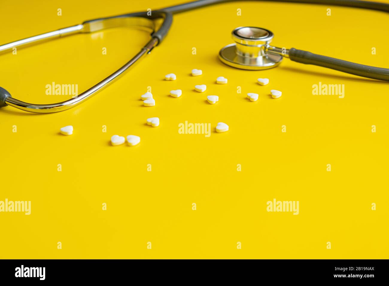 Medizinisches Stethoskop und weiße Herzpillen auf gelbem Hintergrund Gesundheitsminimalismuskonzept Stockfoto