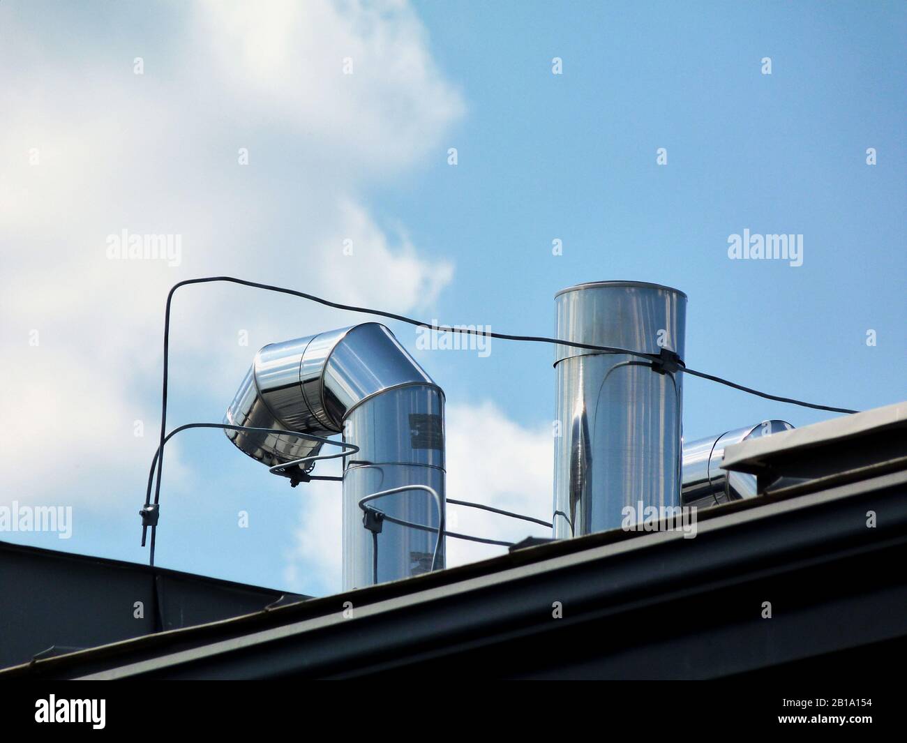 Glänzende mechanische Lüftungsschlitze und Kanäle aus Edelstahl auf geschliftem Dach, Gebäudetechnik, Heizung, Kühlung und Gebäudebelüftung.. Stockfoto