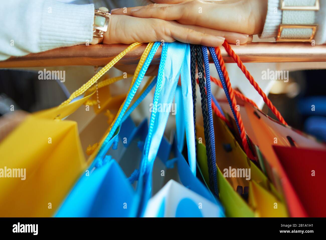 Nahaufnahme der modernen Frau in weißem Pullover und Rock in der Nähe farbenfroher Einkaufstaschen, die an der Kupferschiene hängen. Stockfoto