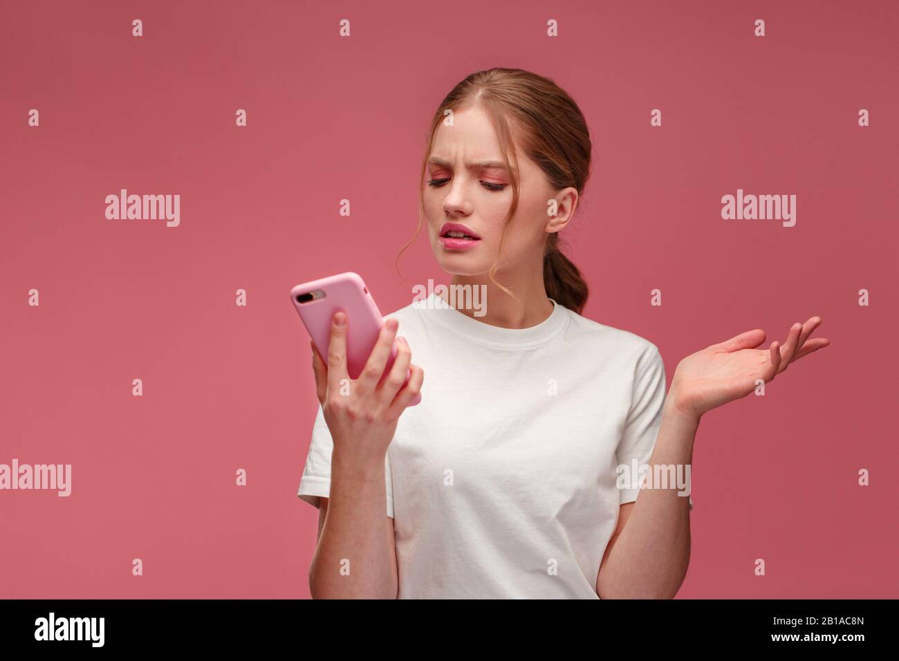 Verwirrte junge Rotkopffrau mit pinkfarbenem Smartphone.Embargierte Mädchen  hat Problem mit kaputtem, nicht funktioniertem Handy.Empfang schlechter  Nachrichten oder E-Mails,Spam Stockfotografie - Alamy