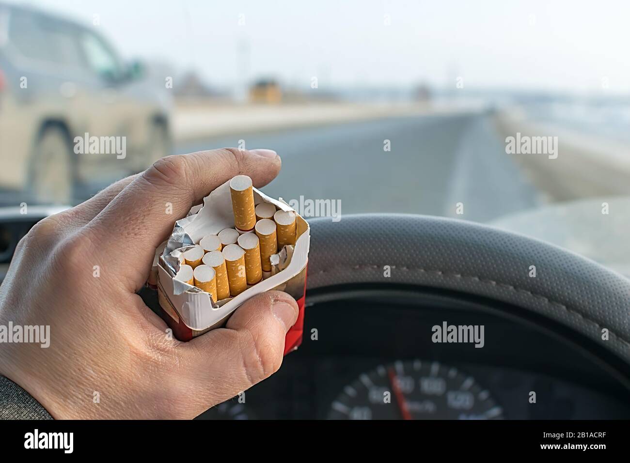 Blick auf die Hand eines Autofahrers, der während der Fahrt auf der Autobahn eine Packung Zigaretten hält Stockfoto