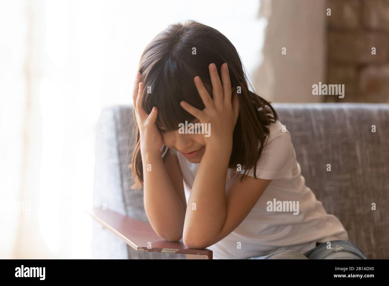 Trauriges kleines Mädchen fühlt sich einsam allein im Sessel sitzen Stockfoto