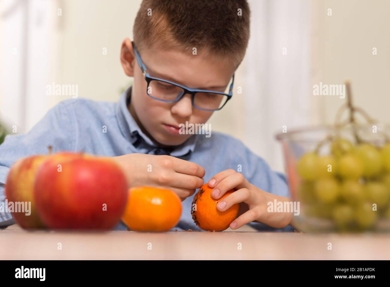 Der Junge mit Brille pflückt Nelken in die Mandarinfrucht. Die tangentiale Frucht mit Nelken von einem schulpflichtigen Jungen garnieren. Im Vordergrund apple und Stockfoto