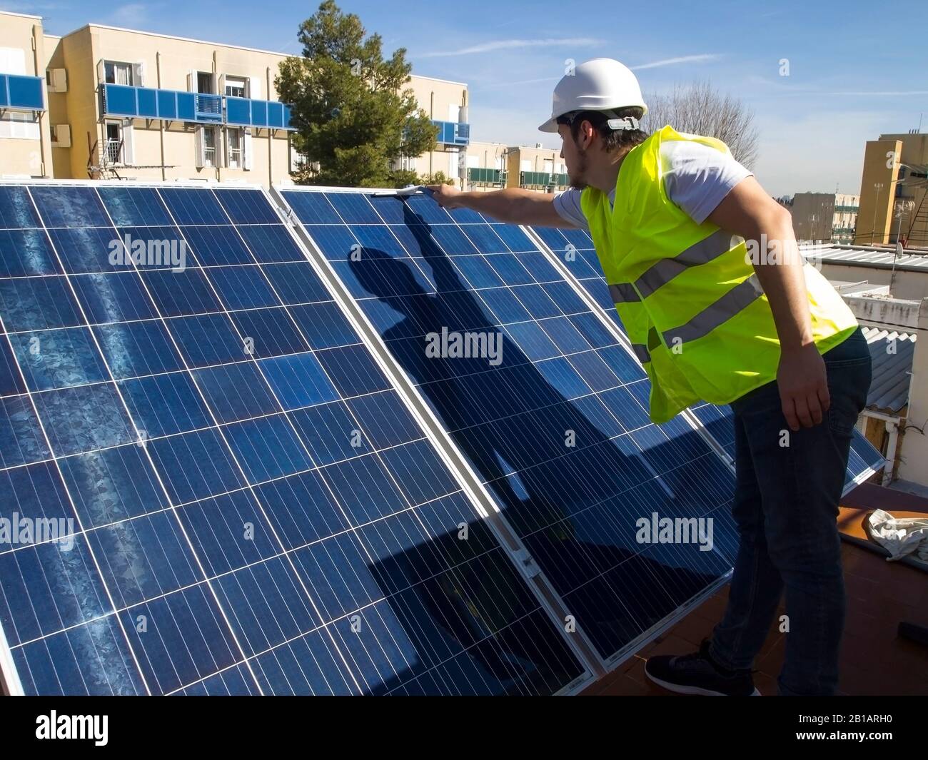 Kaukasisch attraktiver junger Techniker, der Solarpaneele mit einem Glasreiniger säubert. Alternative Stromquelle, nachhaltige Ressourcenkonzeption. Stockfoto