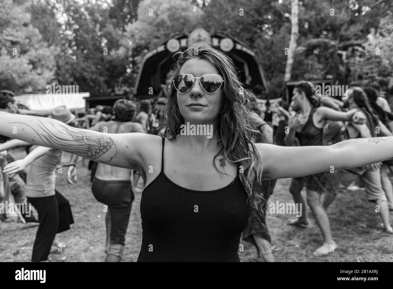Ein kreativer monochromer Blick auf eine gesunde, tätowierte Frau, die auf einem multikulturellen Festival, das Erde und Spiritualität feiert, eine schwarze Weste mit offenen Armen trägt Stockfoto