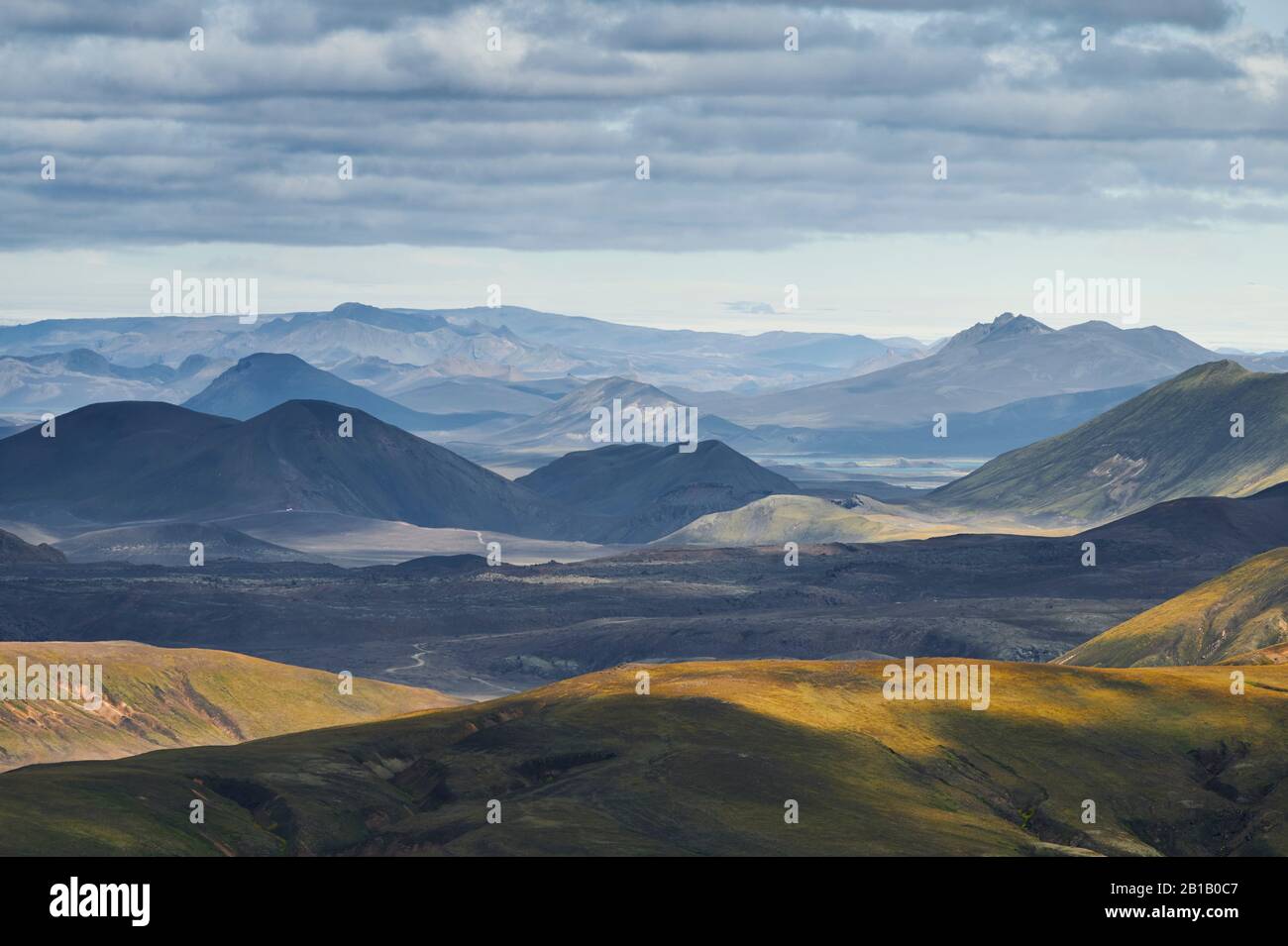 Majestätischer Dronblick auf grüne Hügel und Bergrücken gegen den grau bewölkten Himmel im isländischen Hochland Stockfoto