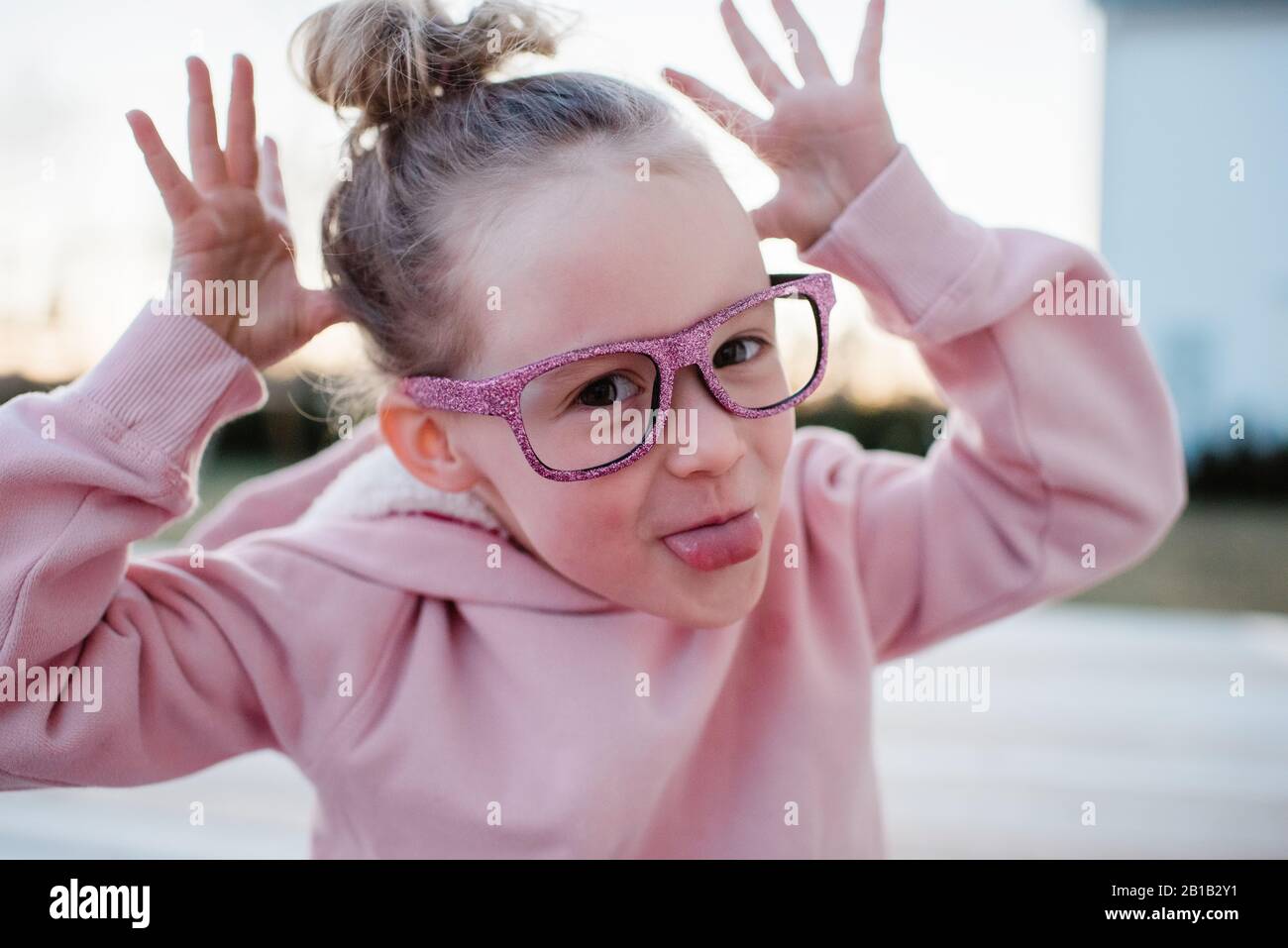 Porträt eines jungen Mädchens, das dumme Gesichter mit funkelnden Gläsern zieht Stockfoto