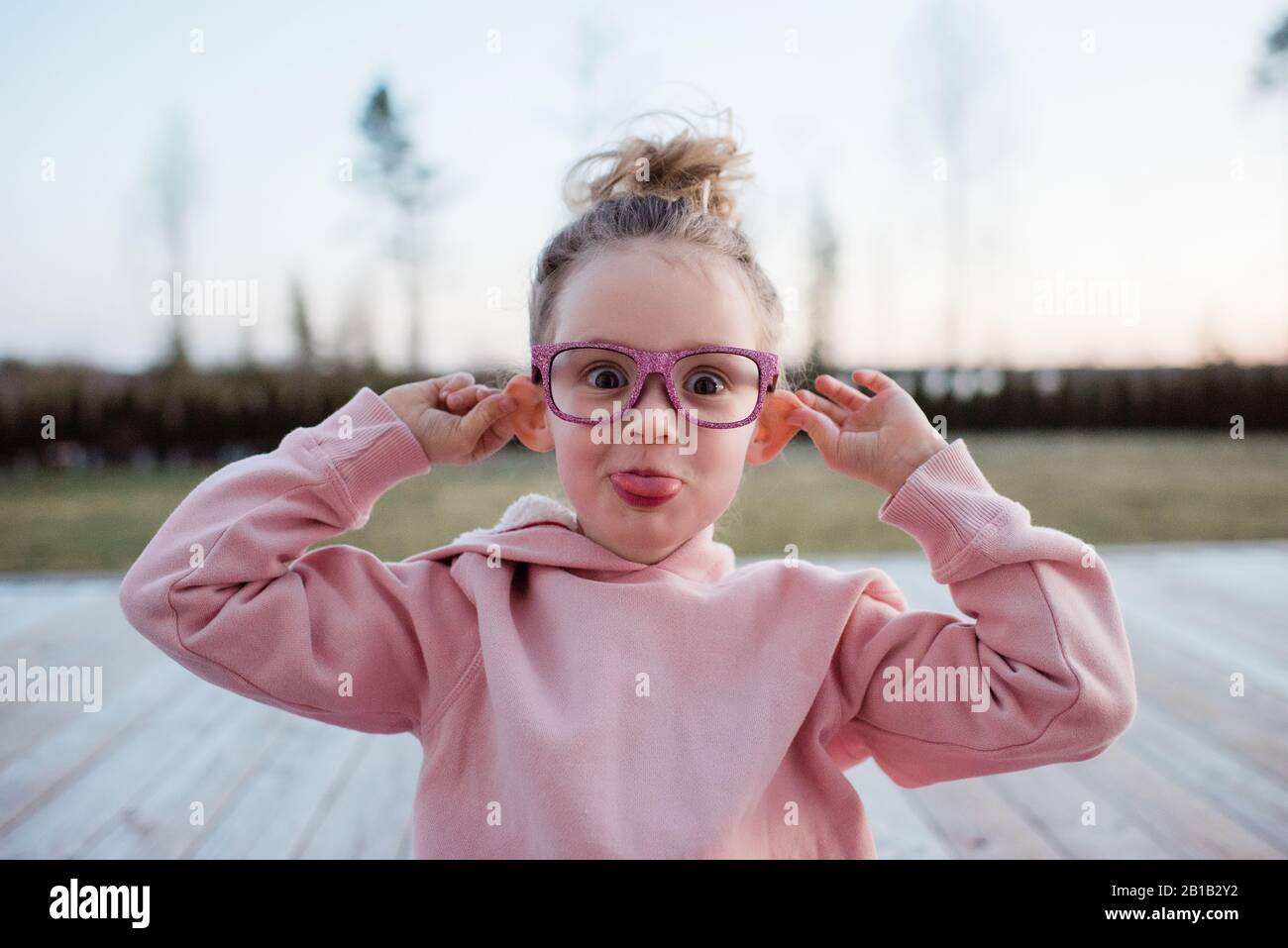 Porträt eines jungen Mädchens, das dumme Gesichter mit rosa funkelnden Gläsern zieht Stockfoto