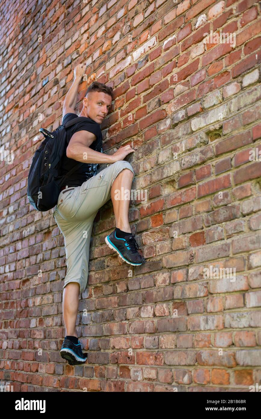 Der Mann klettert an einer Ziegelmauer. Mit Rucksack. Stockfoto