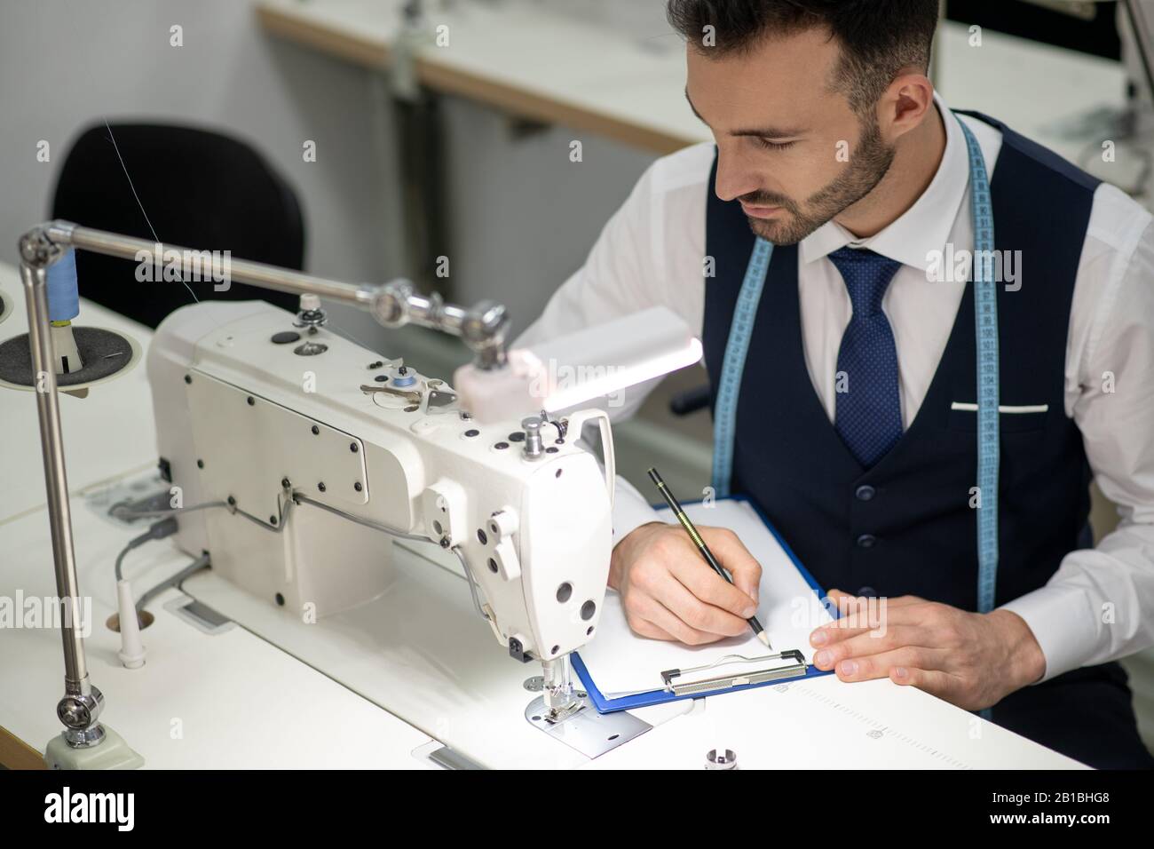 Schneidermännchen sitzt an der Nähmaschine und macht sich Notizen Stockfoto