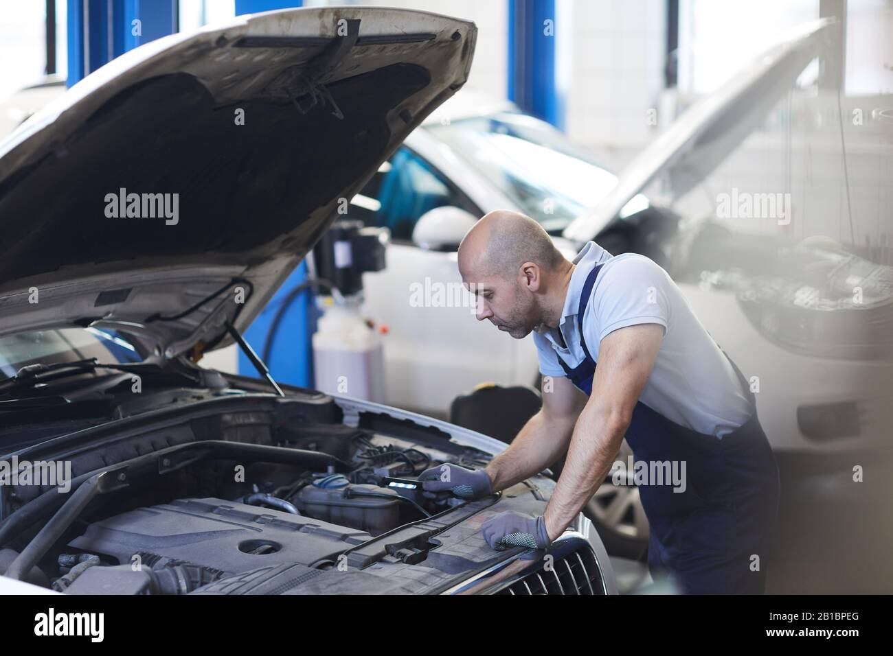 Portrait des muskulösen Automechanikers, der bei der Inspektion im Garagengeschäft in die offene Haube des Fahrzeugs blickt, Kopierraum Stockfoto